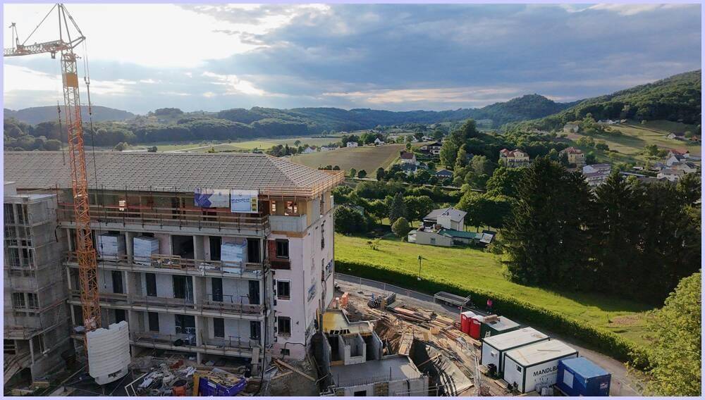 Große Baustelle mit Kran und im Bau befindlichem Gebäude, mit weitem Blick über ein grünes Tal.