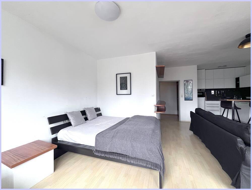 Schlafbereich mit Doppelbett und hellem Laminatboden, offen zum Wohn- und Küchenbereich.