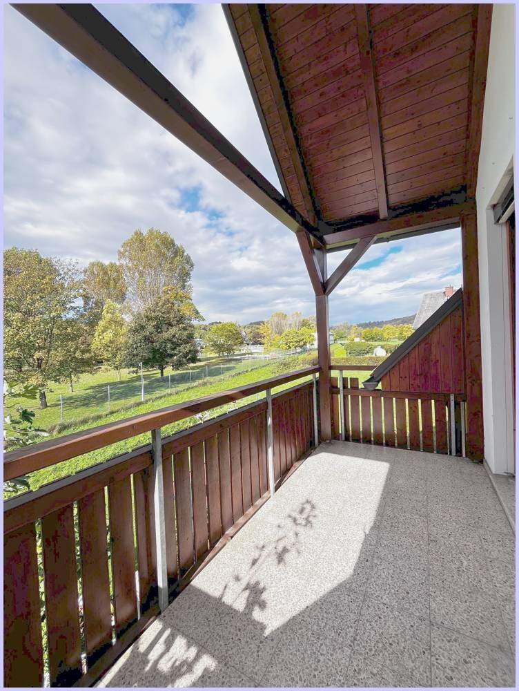 Heller Balkon mit Holzelementen und Panoramablick auf die grüne Umgebung.