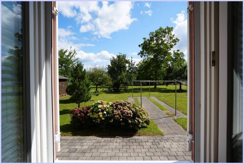 Blick aus dem Fenster auf den gepflegten Garten mit Rasenfläche und blühenden Hortensien.