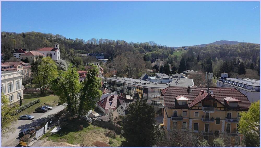 Weitläufige Ansicht einer Siedlung mit moderner und traditioneller Architektur, umgeben von bewaldeten Hügeln.