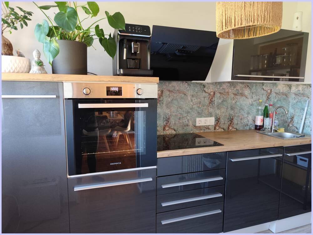 Moderne Küche mit dunklen Hochglanzfronten, Backofen, Spüle und Kochfeld.