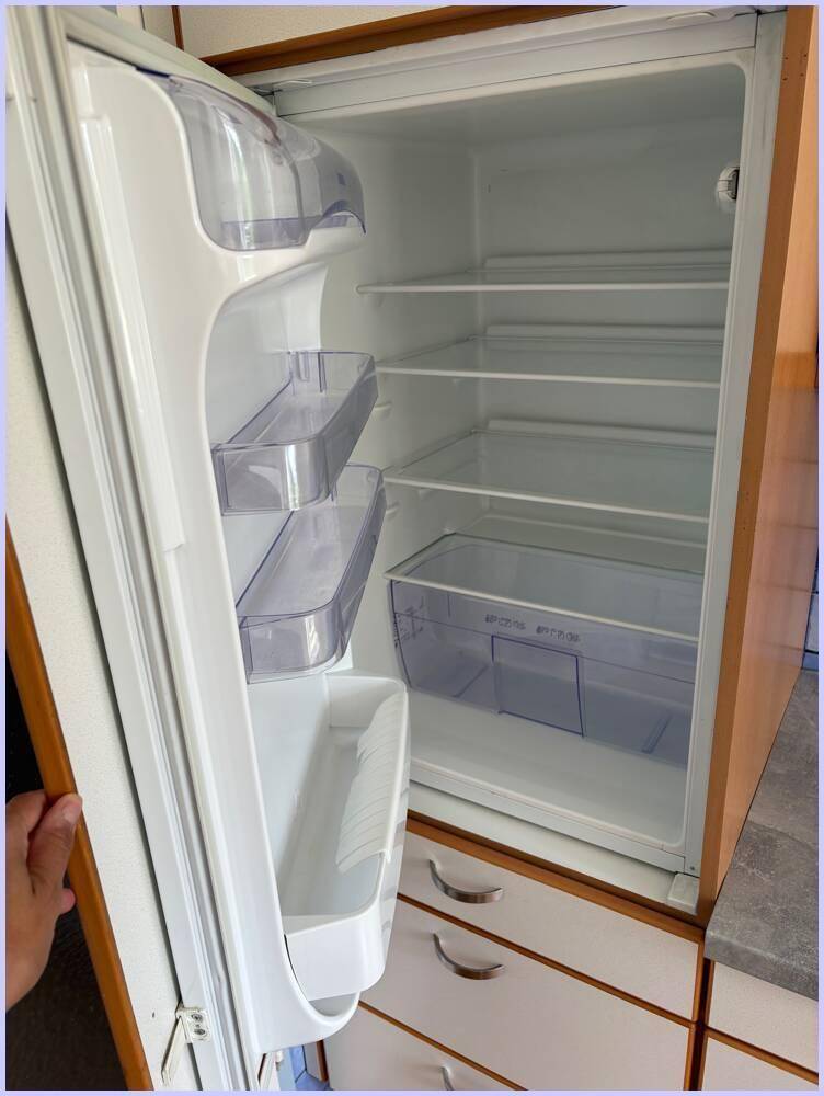 Offener Kühlschrank mit mehreren Fächern und Ablagen, integriert in eine Küchenzeile.