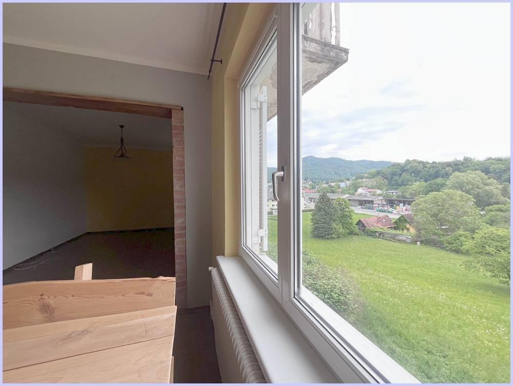 Blick aus dem Fenster auf eine grüne Landschaft mit Hügeln und umliegenden Häusern.