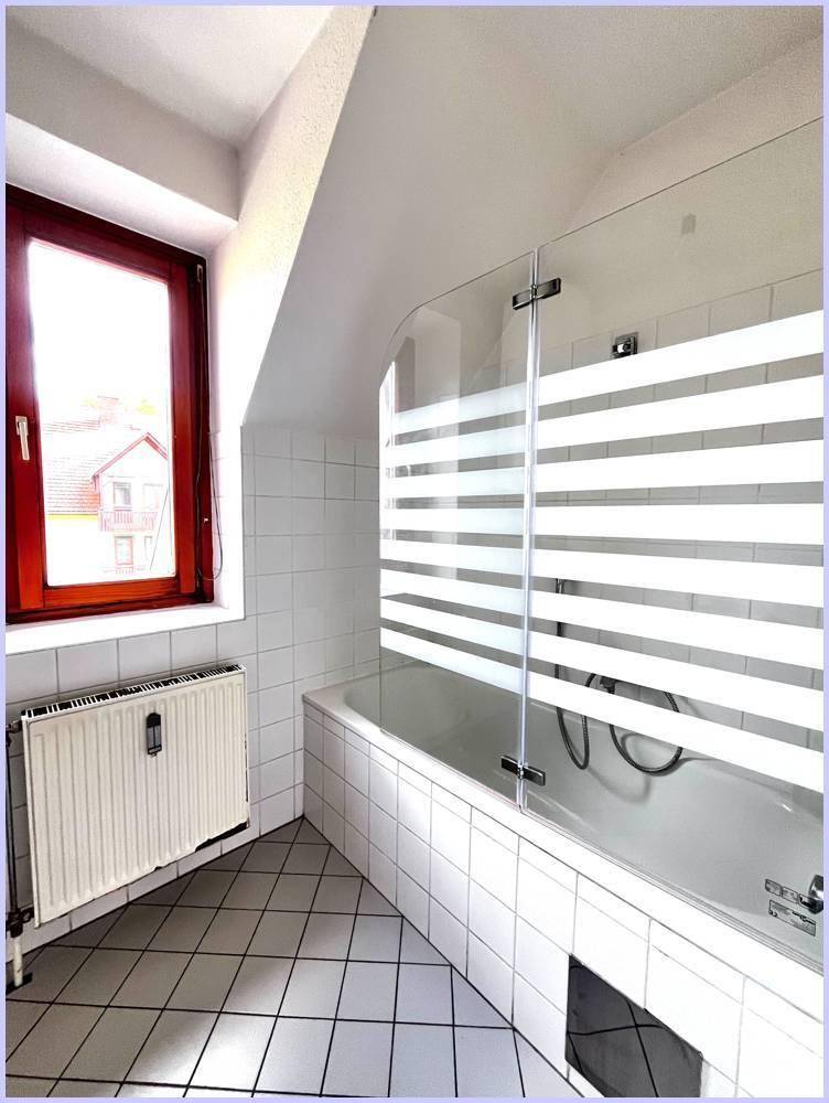 Badezimmer mit Badewanne, Duschabtrennung, Fliesen und Fenster.
