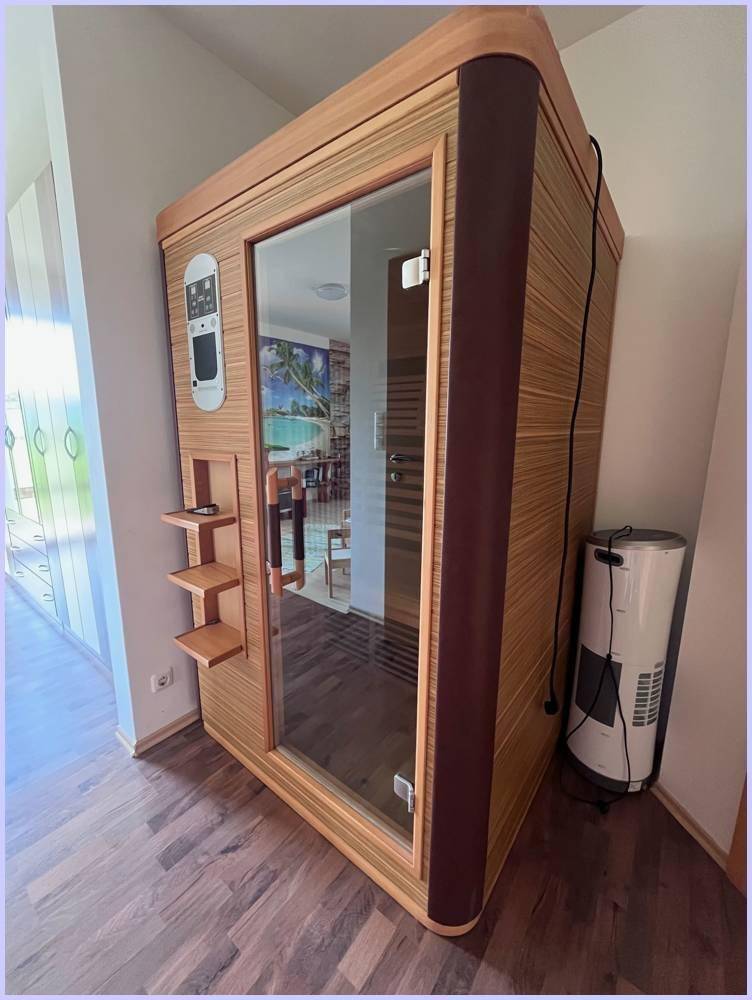 Moderne Infrarot-Saunakabine aus Holz mit Glastür in einem Wohnbereich.