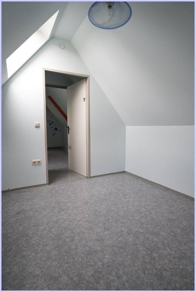 Helles Dachzimmer mit schrägen Wänden, Dachfenster und Zugang zu einem weiteren Raum.