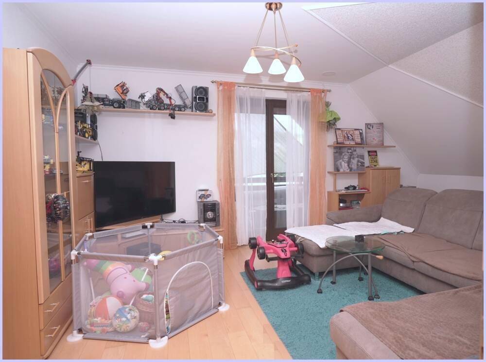 Gemütliches Wohnzimmer im Dachgeschoss mit Sofa, Fernseher und Zugang zum Balkon.