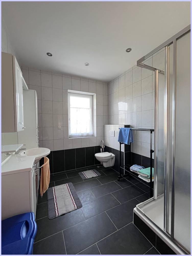 Modernes Badezimmer mit schwarz-weißen Fliesen, Duschkabine und Fenster für Tageslicht.