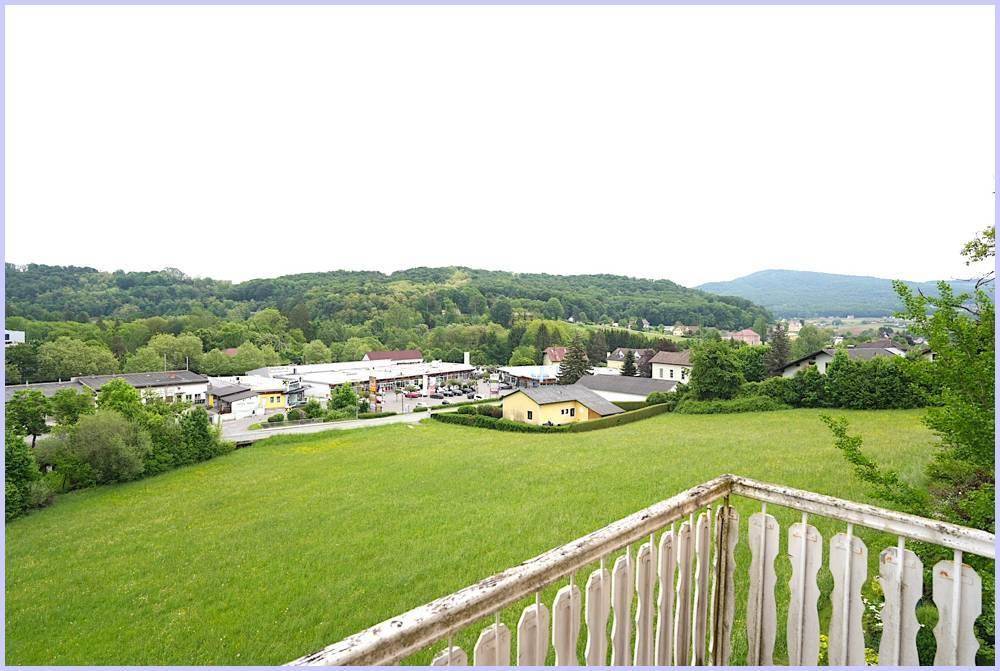 Blick von einem Balkon auf eine grüne Landschaft mit Häusern und Hügeln in der Ferne.