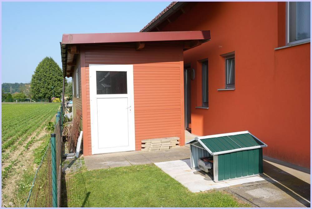 Kleiner Schuppen neben einem Haus mit oranger Fassade, angrenzend an ein Feld.