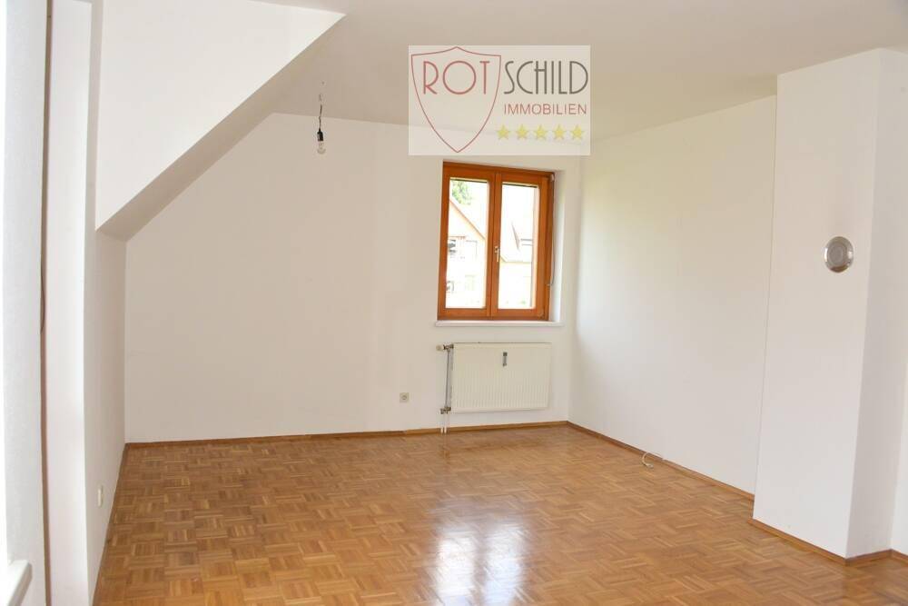 Helles Schlafzimmer mit Parkettboden, Dachschräge und Fenster mit Blick ins Grüne.