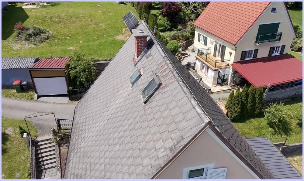 Luftaufnahme eines Hausdaches mit Solarpaneelen, Schornstein und grüner Umgebung.