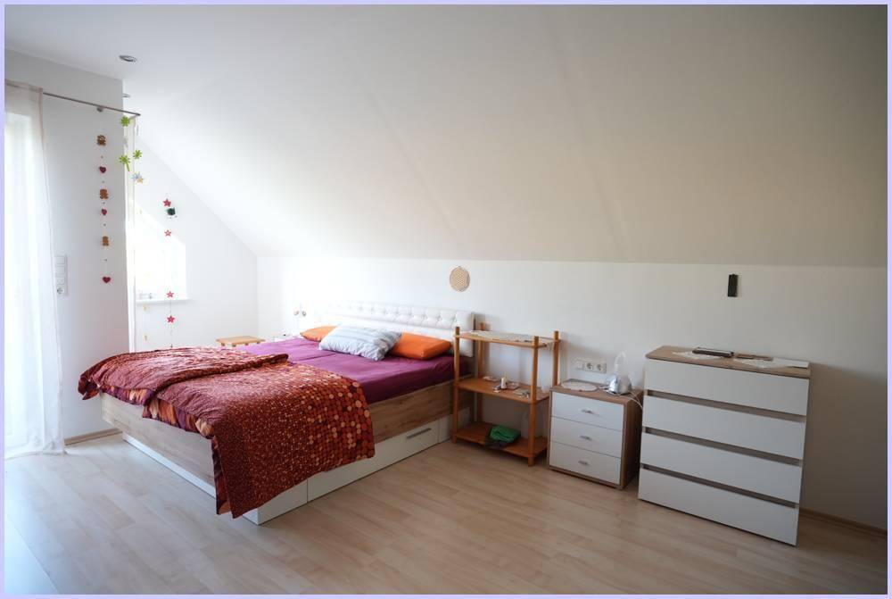 Helles Schlafzimmer im Dachgeschoss mit Dachschräge, Holzboden und Fenster.