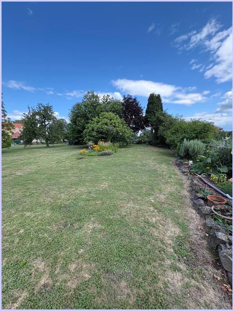Langer Gartenbereich mit Rasen, Blumenbeeten und einer Steinmauer.
