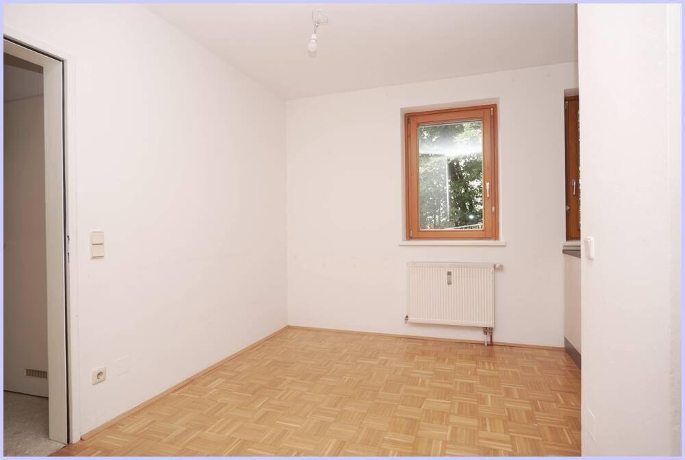 Helles Zimmer mit Parkettboden, großem Fenster und Heizkörper unter dem Fenster.