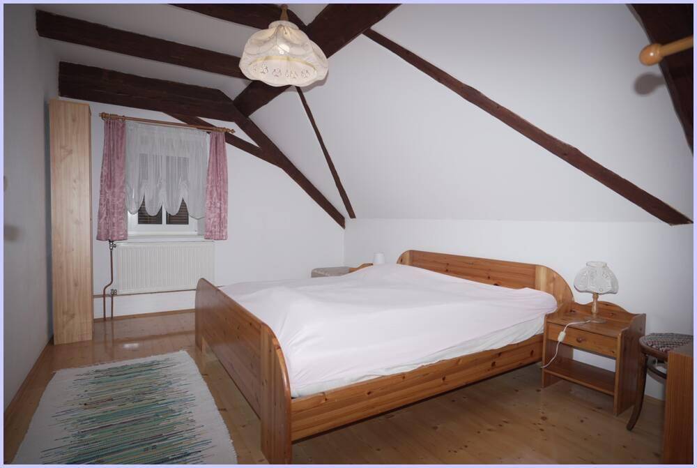 Schlafzimmer im Dachgeschoss mit Holzboden, sichtbaren Holzbalken und einem einfachen Doppelbett.