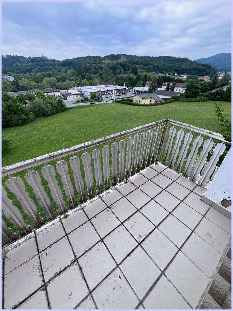 Balkon mit Fliesenboden und weitem Blick über grüne Felder und Berge.