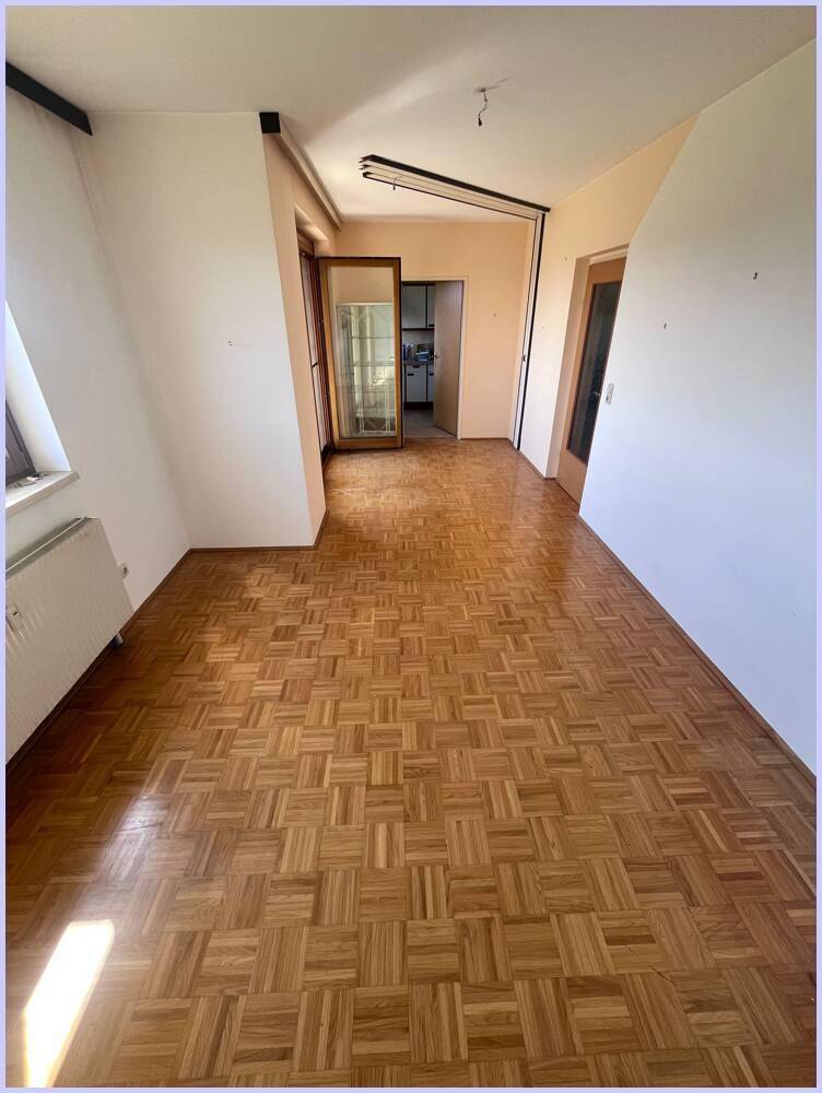 Geräumiges Zimmer mit Parkettboden, weißen Wänden und Zugang zu einem weiteren Bereich.