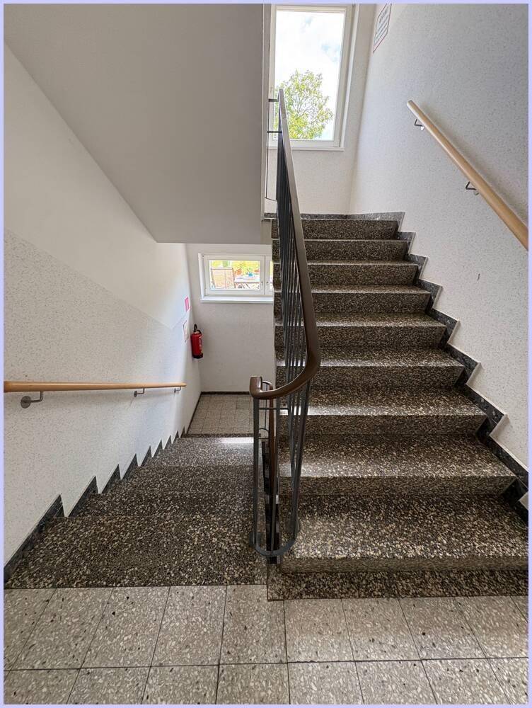 Treppenhaus mit Terrazzostufen, Holzhandlauf und Fenstern für natürliches Licht.