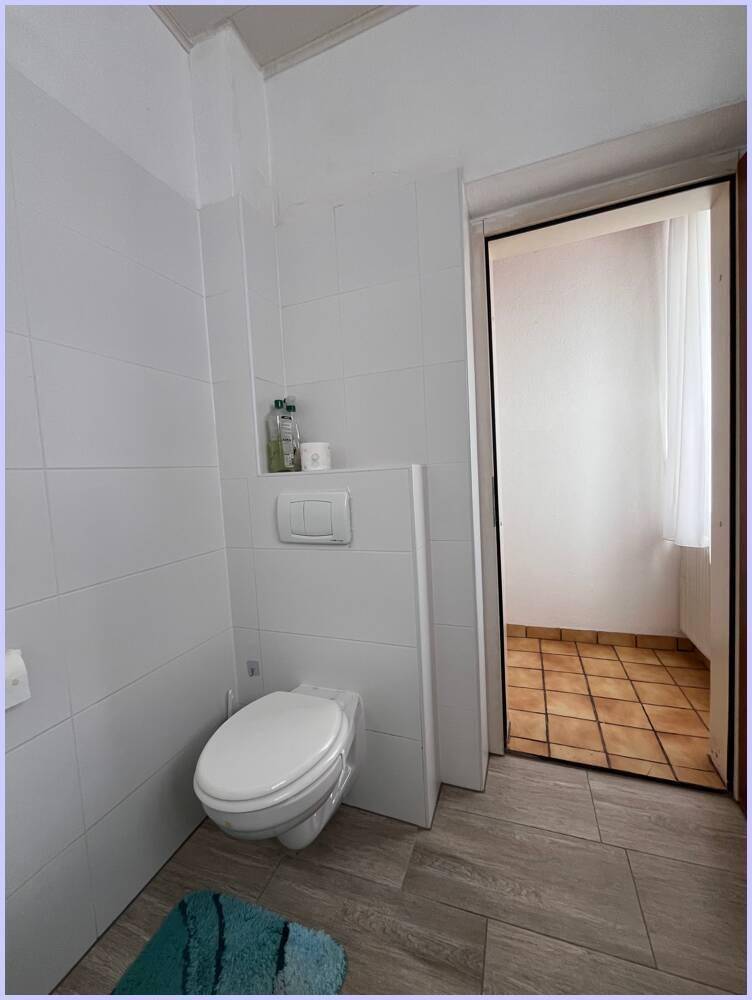 Separate Toilette mit weißen Fliesen und einem kleinen Waschbecken, die funktional und hell ist.