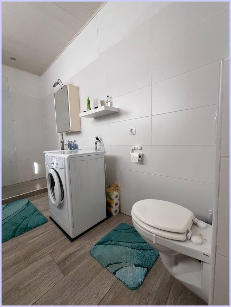 Helles Badezimmer mit modernen Fliesen, begehbarer Dusche und Toilette, das funktional und sauber wirkt.
