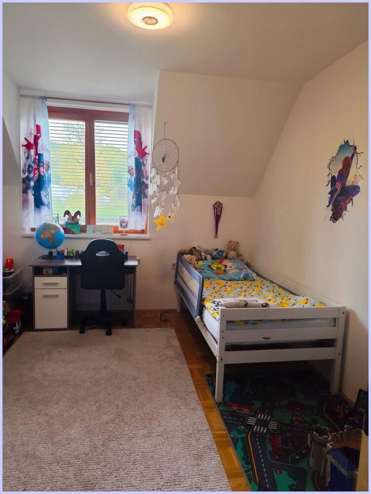 Kinderzimmer mit Bett, Schreibtisch, Teppich und Dachschräge.