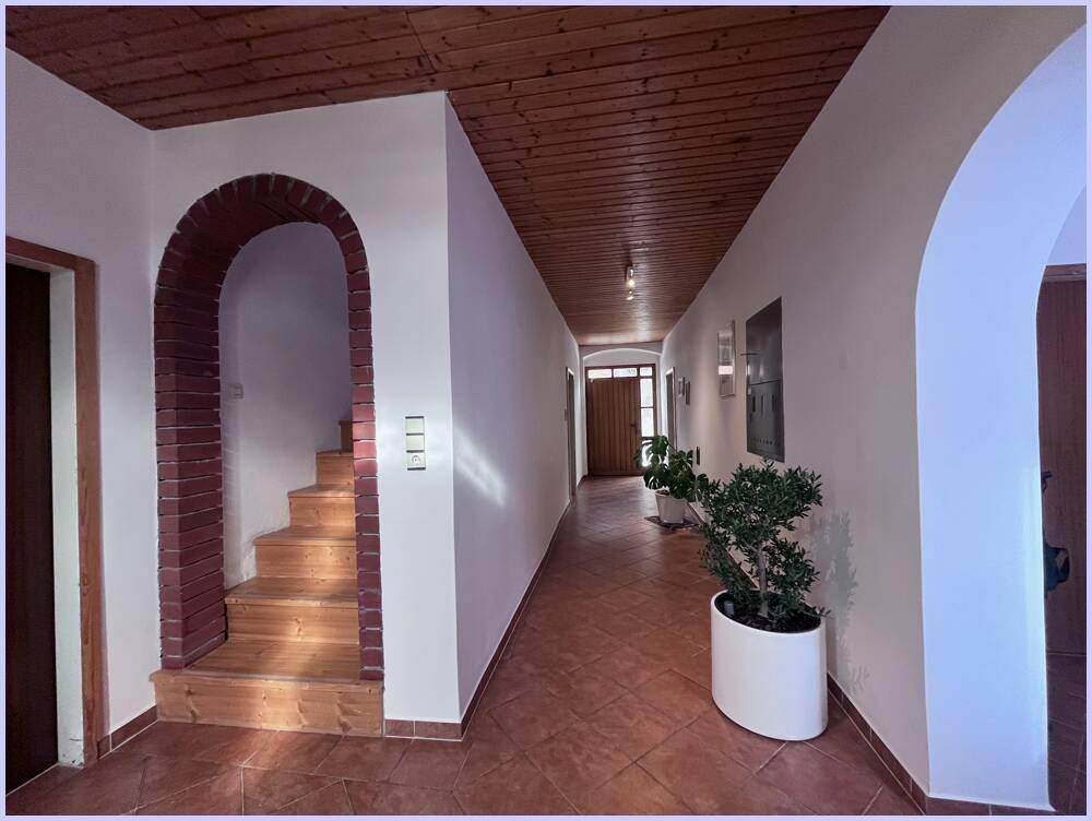 Langer Flur mit Terrakottafliesen, Holzdecke und einem gemauerten Bogen, der zu einer Treppe führt.