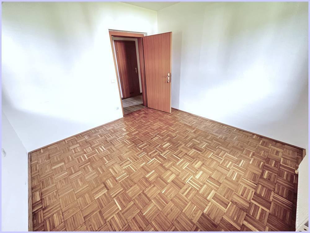 Leeres Schlafzimmer mit Parkettboden und Holztür, bereit zur Einrichtung.