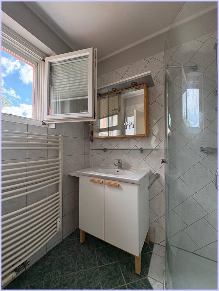Modernes Badezimmer mit Duschkabine, Waschbecken und Fenster für Tageslicht.