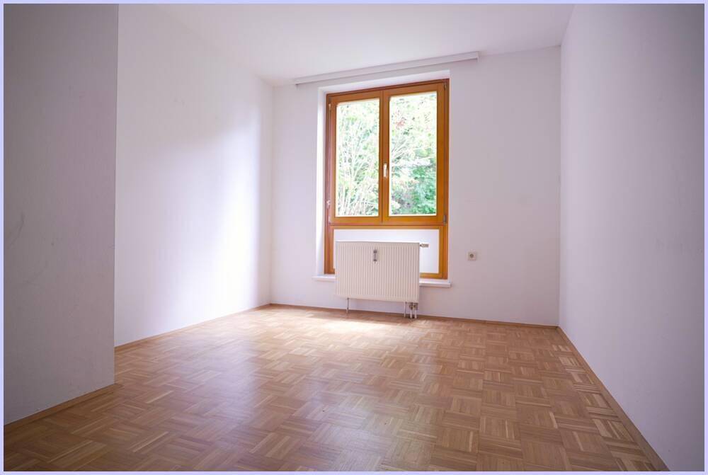 Freundliches Zimmer mit Parkettboden, großem Fenster und Blick ins Grüne.