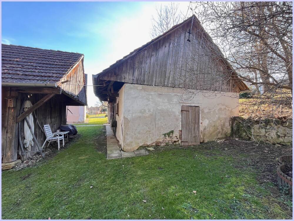 Kleines Nebengebäude mit verputzter Fassade und Holztür, umgeben von Rasen und Bäumen.