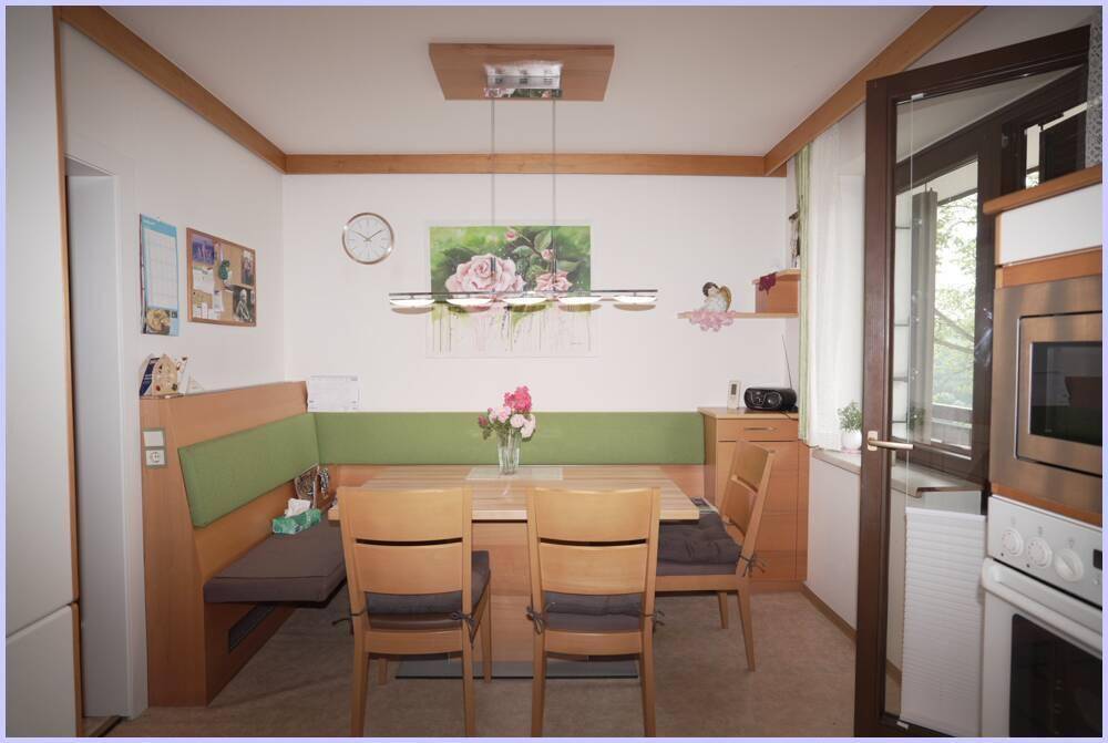Gemütliche Essküche mit Holztisch, Eckbank und Blick ins Grüne durch das Fenster.