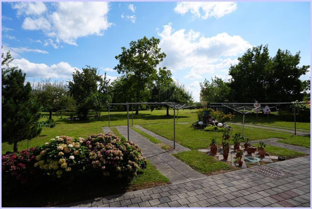 Weitläufiger Garten mit Rasenflächen, Wäscheleinen und blühenden Pflanzen.