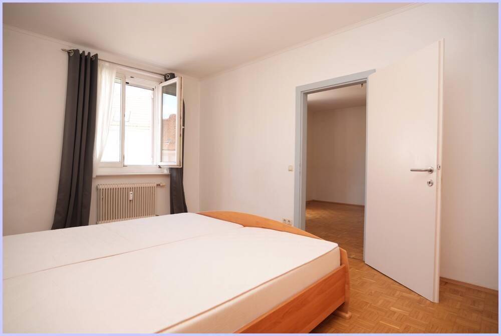 Schlafzimmer mit Doppelbett, Parkettboden und Fenster für natürliche Belichtung.
