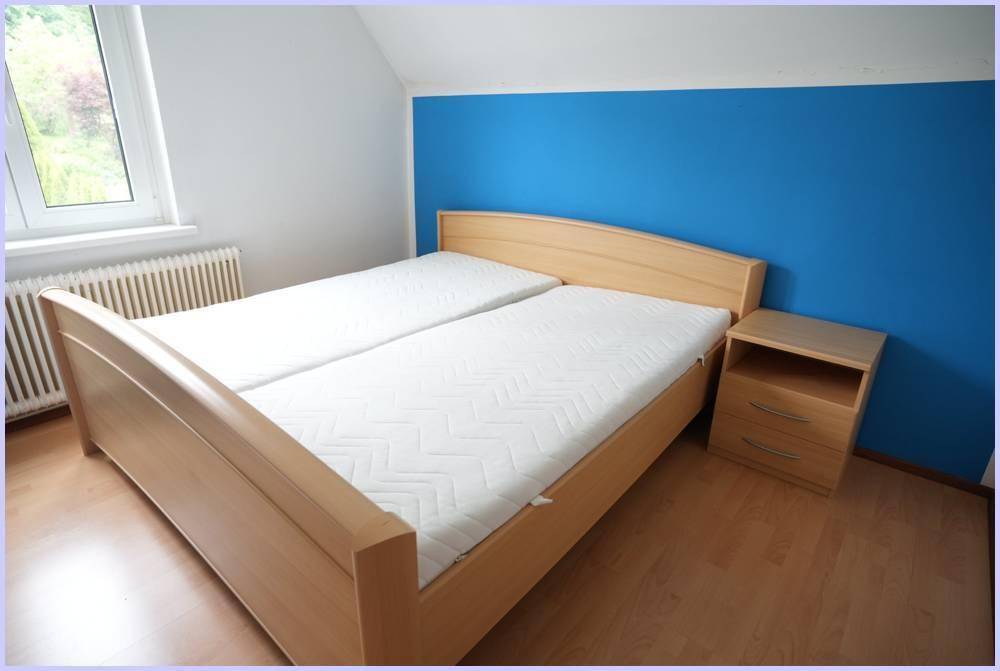 Schlafzimmer mit hellem Holzdoppelbett, Nachttisch und einer blauen Akzentwand.