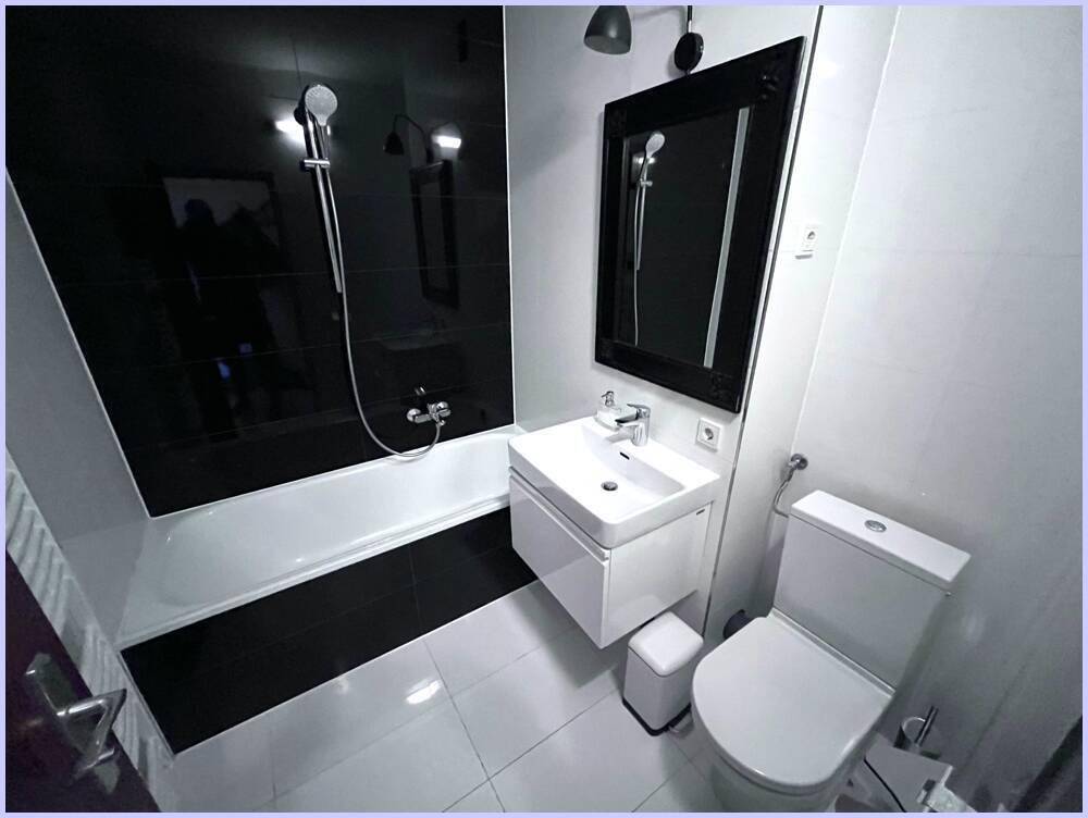 Stilvolles Badezimmer mit Badewanne und modernem Waschtisch, akzentuiert durch schwarze Fliesen.