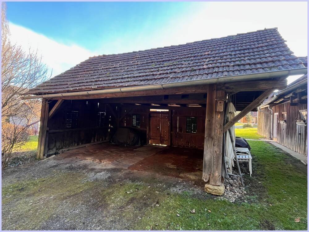 Offener Holzschuppen oder Carport mit Ziegeldach, der als Unterstand oder Lagerraum dienen könnte.