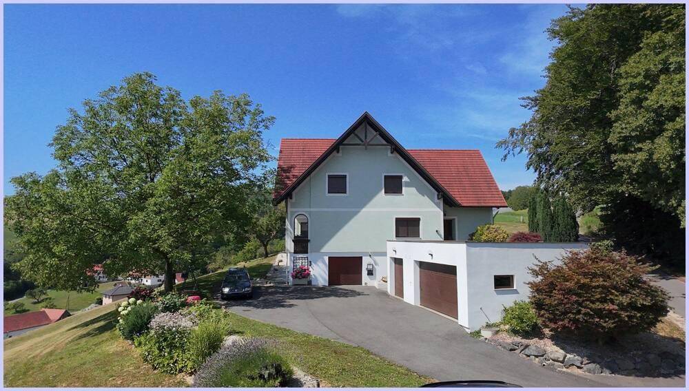Vorderansicht des Hauses mit hellgrüner Fassade, rotem Dach und integrierten Garagen sowie einer Auffahrt.