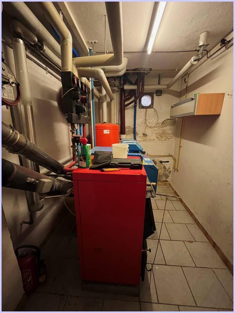 Geräumiger Heizungsraum mit umfangreicher Rohrinstallation, Heizkessel und gefliestem Boden.