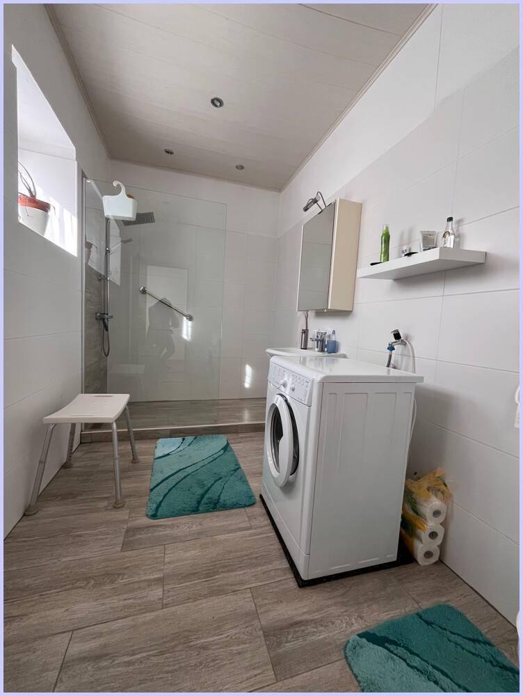 Modernes Badezimmer mit begehbarer Dusche, weißen Fliesen und Waschmaschine, das hell und funktional ist.