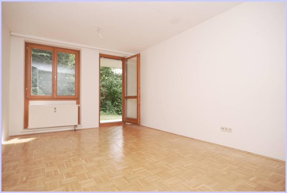 Geräumiges Zimmer mit Parkettboden und Zugang zu einem Außenbereich mit viel Grün.