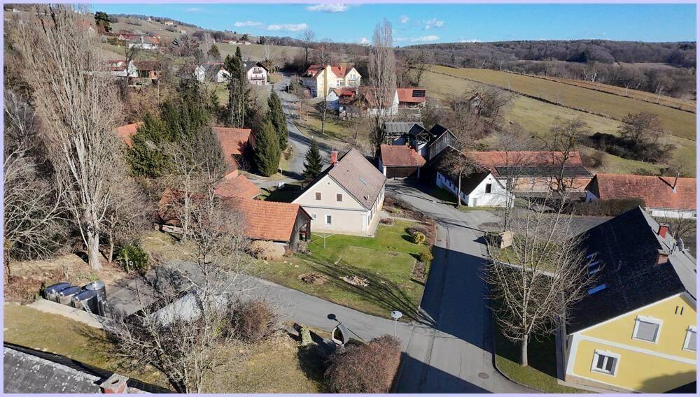 Luftaufnahme einer ländlichen Siedlung mit verschiedenen Häusern, Straßen und weiten Feldern im Hintergrund.