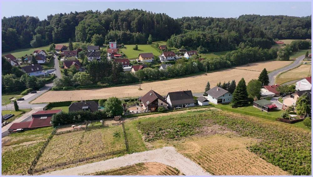 Übersicht über eine ländliche Gegend mit Feldern, Wohnhäusern und einem Waldstreifen am Horizont.