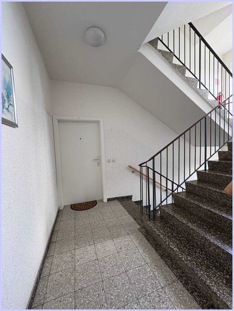 Treppenhaus mit Terrazzoboden, weiß gestrichenen Wänden und einem schlichten Geländer.