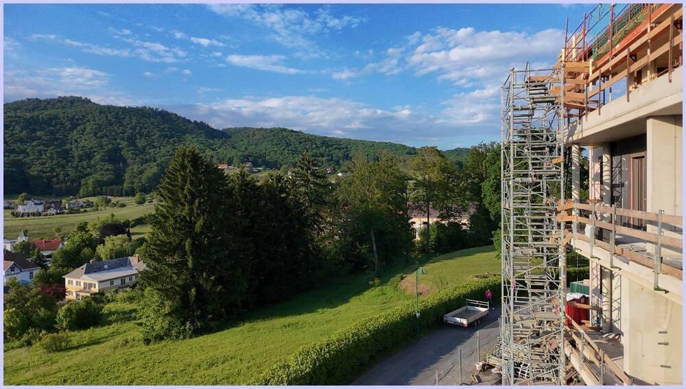 Baustelle mit Gerüst und Blick auf eine grüne Hügellandschaft und entfernte Häuser.