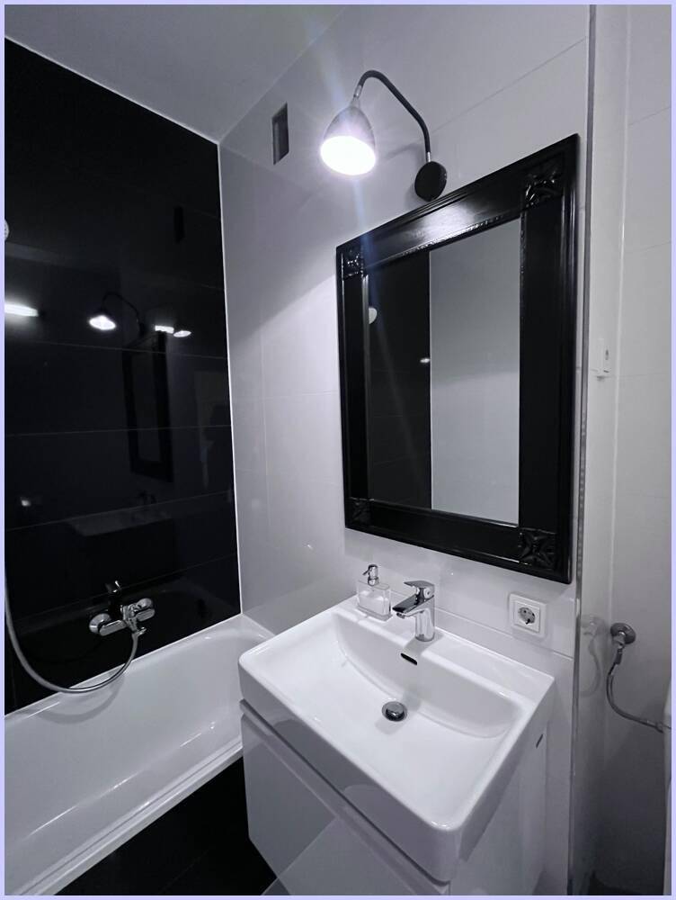 Elegantes Badezimmer mit Waschtisch, Spiegel und Badewanne, in einem zeitlosen Schwarz-Weiß-Design.