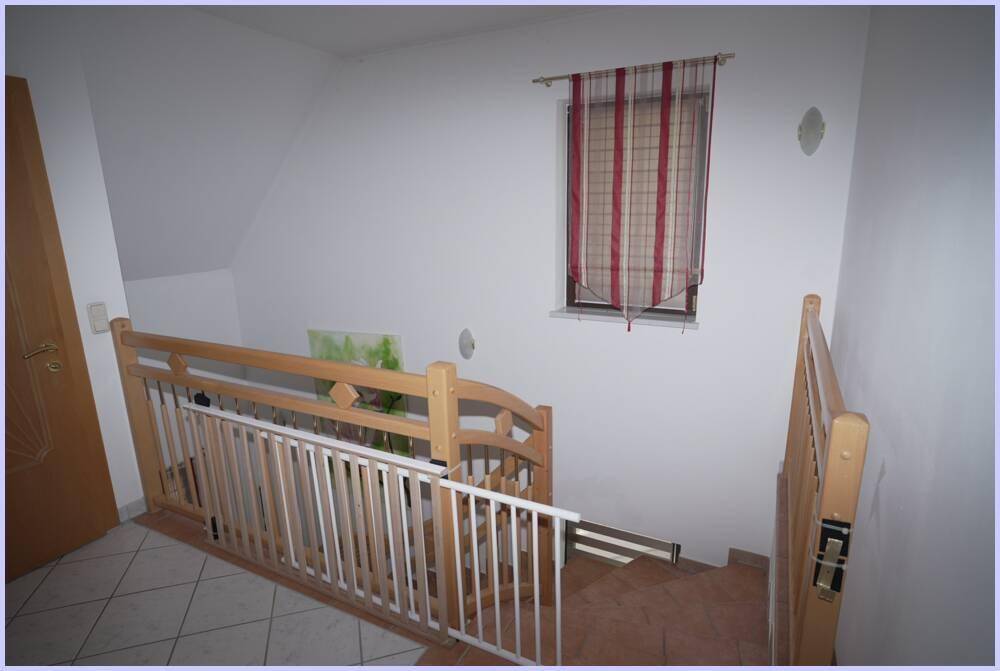 Treppenaufgang mit Holzgeländer und Kindersicherung, beleuchtet durch ein kleines Fenster.