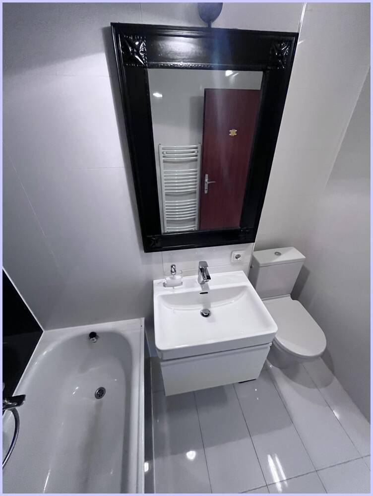Waschtisch mit Spiegel und Badewanne in einem modernen Badezimmer mit klaren Linien.