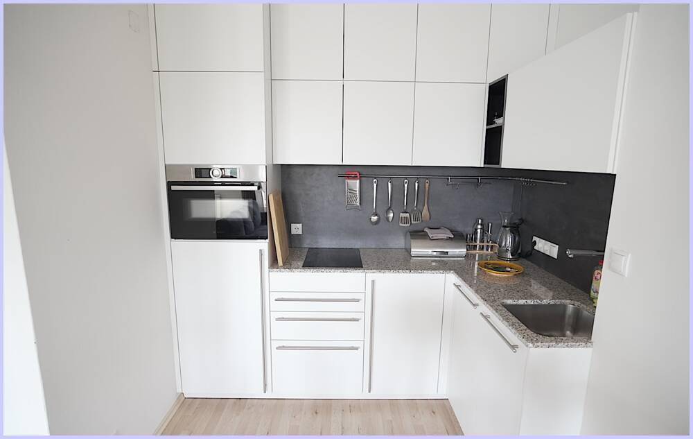 Kompakte, moderne Küche mit weißen Fronten, Induktionskochfeld und integrierten Geräten.